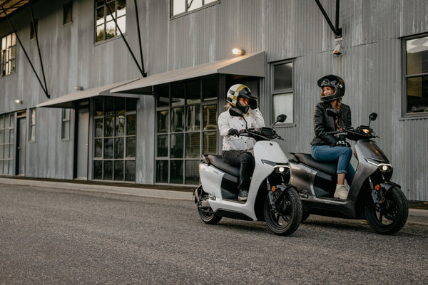Two riders on Zero LS1 scooters outside an industrial building